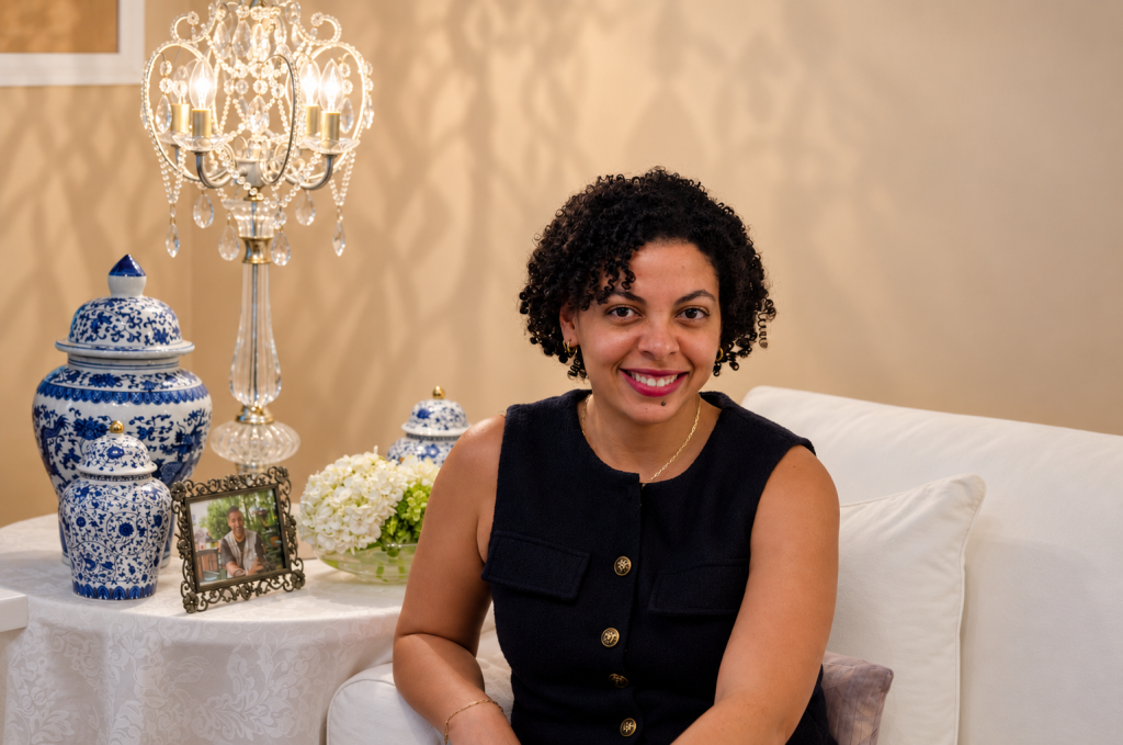 Liza-Marie, COO and co-founder of Hydrangea & Hue Elegant Events, smiling while seated beside blue-and-white porcelain and a crystal chandelier.